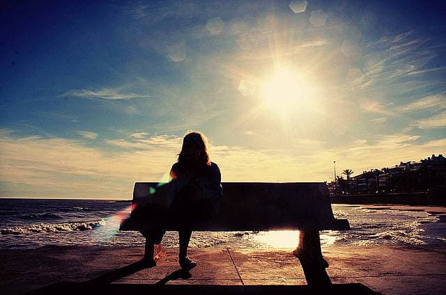 太陽の光を浴びながらベンチに座る女性の画像