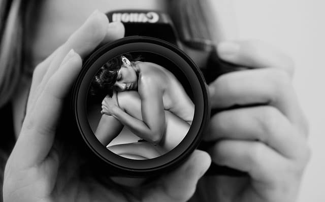 女性が構えるカメラのレンズに裸の女性が映っている画像