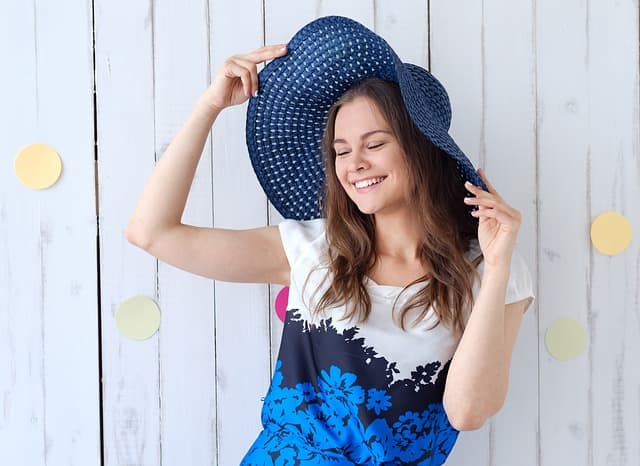 紺色の大きな麦わら帽子を被って笑う女性の画像