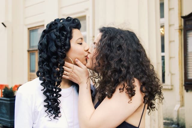 巻き髪の2人の女性がキスしている画像