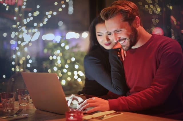 ひとつのパソコンを2人で見つめながら微笑んでいるカップルの画像