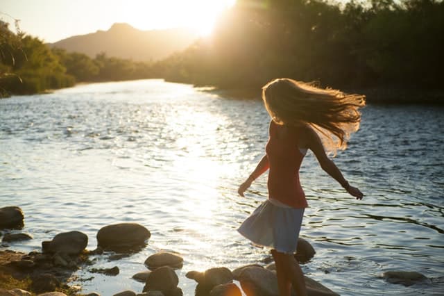 少女が岩をジャンプしながら川遊びをしている画像