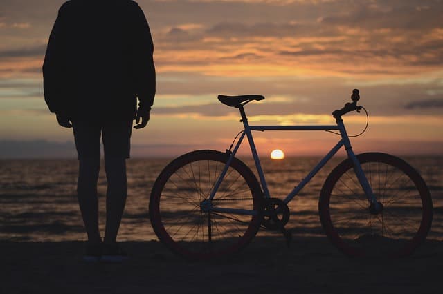 若者が自転車とともにビーチで日の出を一緒に見ている画像