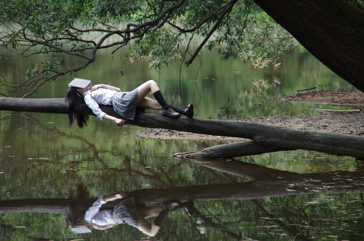 制服を着た少女が顔に本を乗せ湖で休んでいる画像