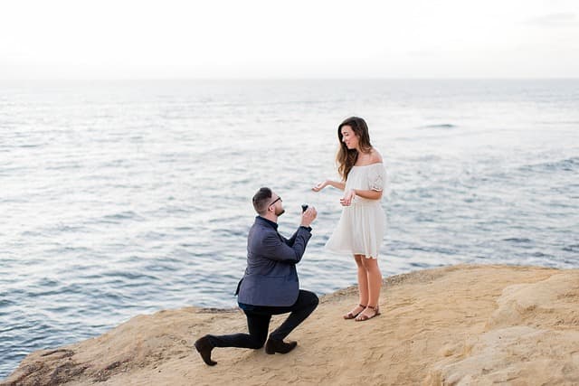 海辺で男性がモテる女性に告白・プロポーズしている画像